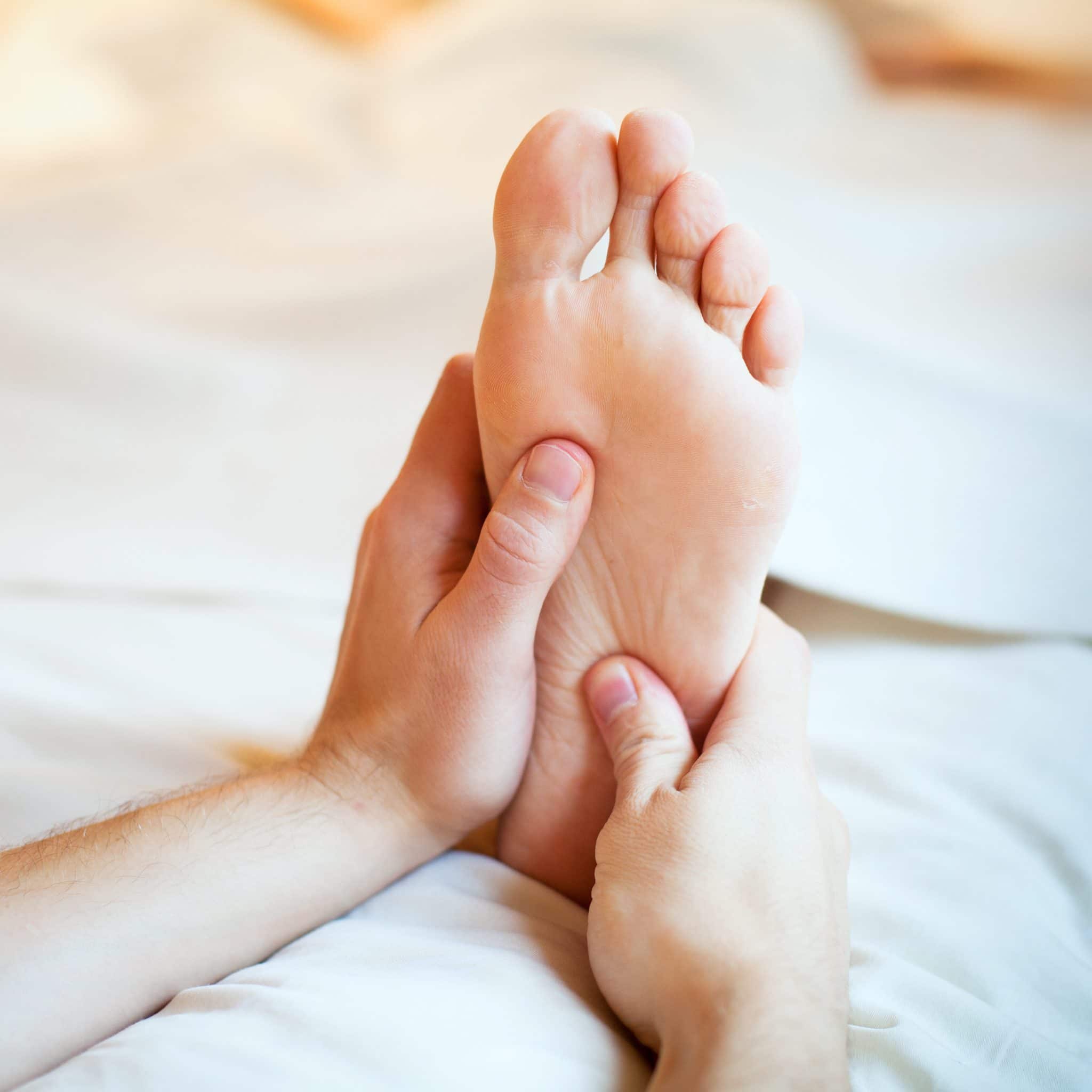 What causes restless legs: hands massaging a foot on a white duvet