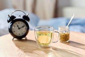 A cup of chamomile tea and an alarm clock on a bedside table